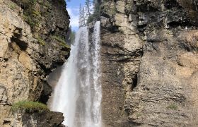 Ein Wasserfall im Johnston Canyon in Kanada. Man sieht zwei Felswände, zwischen denen das Wasser runterfällt. Zwischen den Felsen sieht man noch ein Stück blauen Himmel.