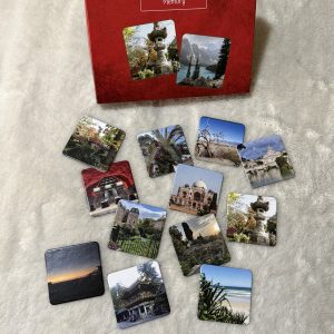 Memory Spiel mit Kärtchen aus allen Teilen der Welt. Der Karton ist rechteckig und rot, auf der Vorderseite sieht man zwei der Spielkarten abgebildet. Er steht aufrecht im Hintergrund auf einem weißen, fellartigen Untergrund. Davor liegen 12 Memorykärtchen mit unterschiedlichen Landschaftmotiven.