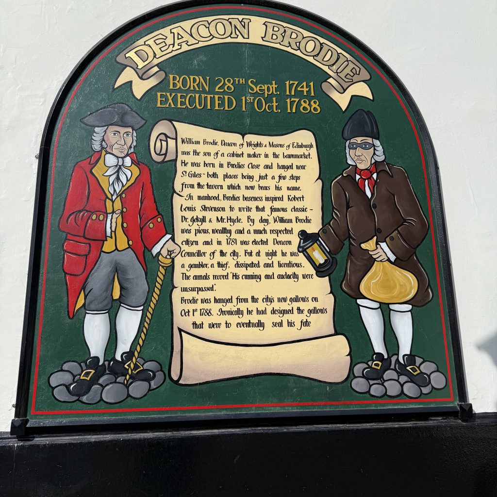 Eine Tafel an einem Pub in Edinburgh erinnert an Brodie. Man sieht zwei Männer die neben einer Schriftrolle stehen. Darauf ist die Geschichte aufgeschrieben.