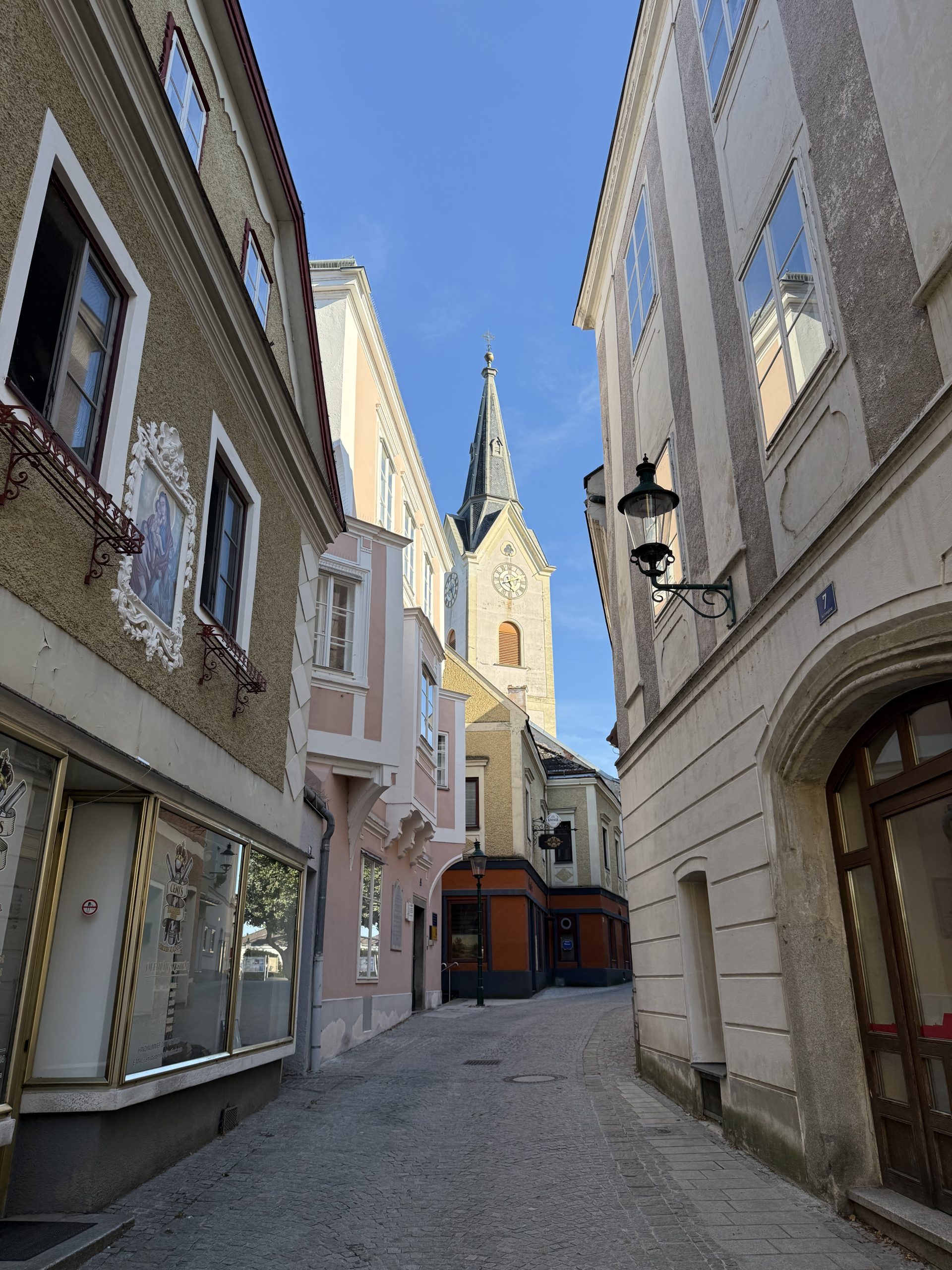 Ybbs is a small town in Lower Austria. You can see a narrow alley with a church at the end of it. The houses are beautifully designed, some even featuring paintings on the facade or stucco. 