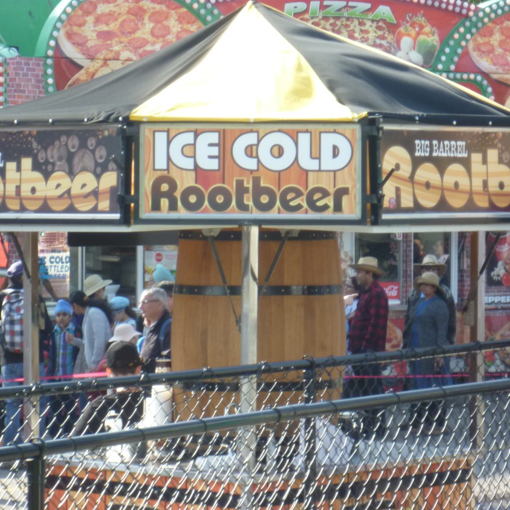 Ein Rootbeer Stand am Stampede. Man sieht ein großes Holzfass, darüber ein Schirm mit der Aufschrift "Ice Cold Root Beer"