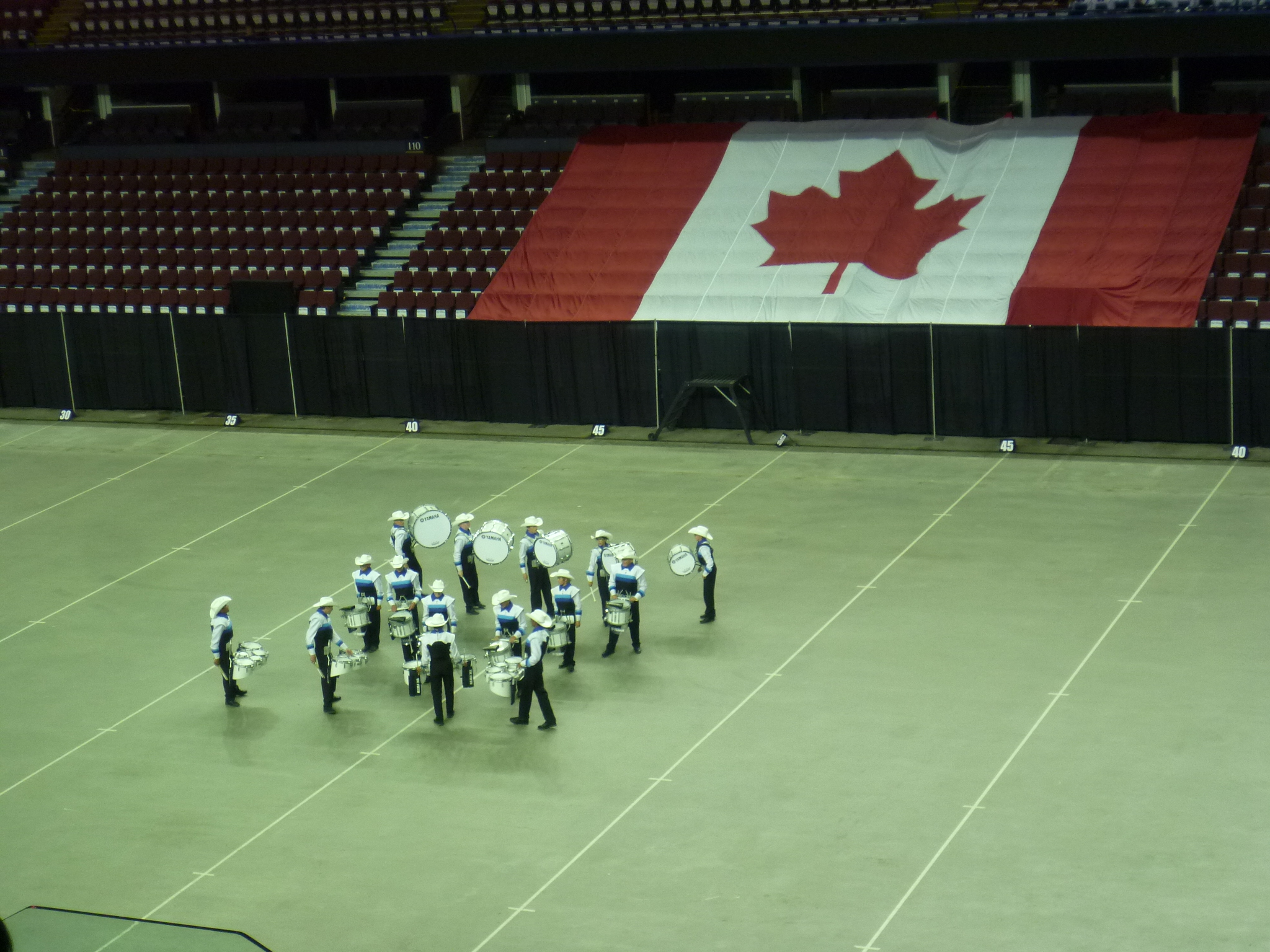 Man sieht einen Sportplatz mit der kanadischen Flagge und auf dem grünen Feld einige Musiker in Uniform